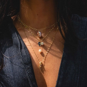 Close-up of layered 14k gold-plated necklaces with pearl, enamel, and zircon charms