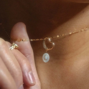 Detail of 18K gold necklace featuring a heart clasp and oval opal pendant on a model