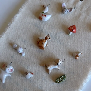 Close-up view of various handmade forest style ceramic animal pendants on beige fabric background
