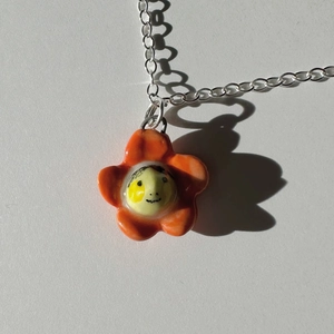 Macro shot of an orange and yellow flower pendant necklace with a smiling face