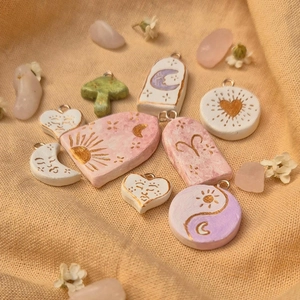 Handmade clay pendants with gold sun and moon patterns in pastel colors on warm fabric
