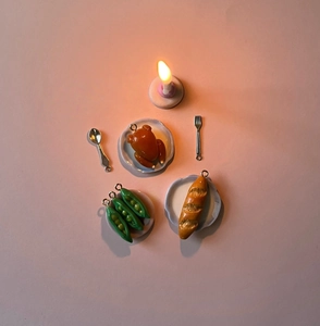 Detailed macro view of 18K gold miniature food charms with tiny dinnerware and candle