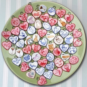 Handcrafted ceramic pendants with animal illustrations and 18K gold hooks in a green tray