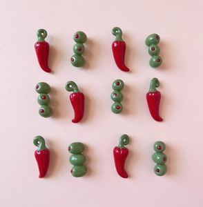 Macro detail of chili and olive pendants in polished resin on a soft pink background