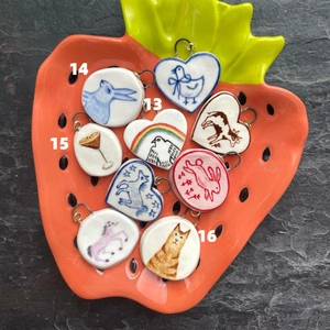 Artistic handmade ceramic pendants with animal drawings in a bright orange strawberry plate