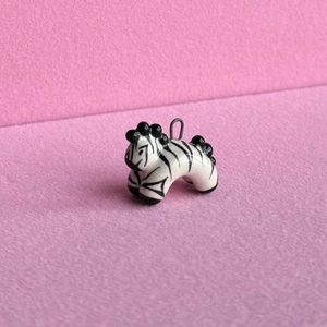 Close-up of a handcrafted zebra pendant with black stripes on soft pink background