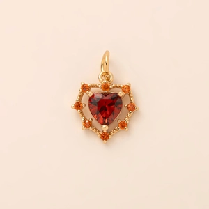 Macro detail of heart-shaped gold pendant with red gemstone and orange accent stones