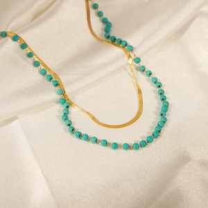 Double-layered turquoise beaded and gold snake chain necklace on white satin fabric