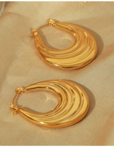 Macro detail of gold teardrop earrings featuring a textured wavy surface and latch closure