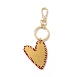 Detail eines goldenen Herzanhängers mit roter Naht und Karabinerverschluss für Taschen