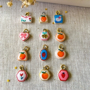 Makroaufnahme handbemalter Keramik-Anhänger mit Blumen- und Fruchtmotiven und Goldösen