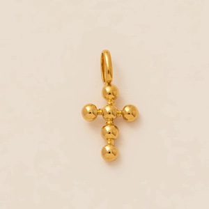 Detailed macro shot of golden bead cross pendant with polished finish on beige surface