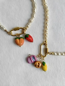 Détail de colliers de perles blanches ornés de breloques colorées en forme de fruits