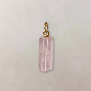 Detail van een rechthoekige roze kristallen hanger met een gouden metalen ring op grijze basis