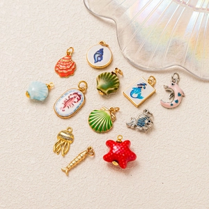 Collezione di pendenti marini placcati oro 14k con creature in smalto su fondo chiaro