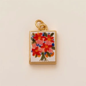 Macro shot of rectangular gold-edged pendant with colorful floral art on white texture