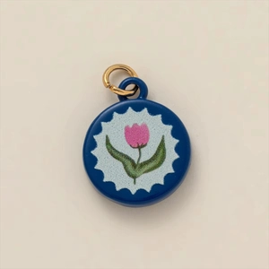 Macro detail of a round enamel pendant featuring pink tulips and golden jump ring attachment