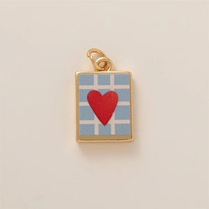 Détail macro du pendentif carré doré avec motif à carreaux bleus et breloque cœur rouge