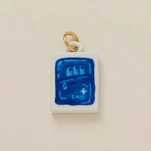 Detalle de un colgante rectangular de cerámica blanca con dibujo azul y anillo dorado