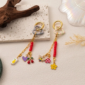 Détail de breloques DIY dorées 18K avec fruits en émail, abeilles et perles rouges sur anneau