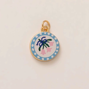 Dettaglio del ciondolo dorato rotondo con mughetto rosa dipinto e fiocco blu elegante