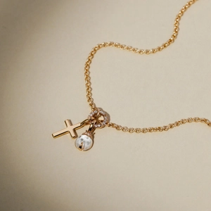 Detail of gold necklace with cross, crystal ring, and pear-shaped gemstone pendant
