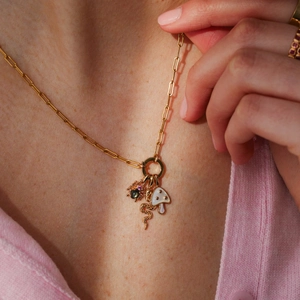 Gold charm necklace with spider snake and mushroom pendants on a pink cardigan model