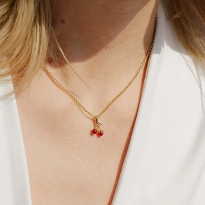 Close-up of a gold cherry pendant necklace with red beads worn by a female model