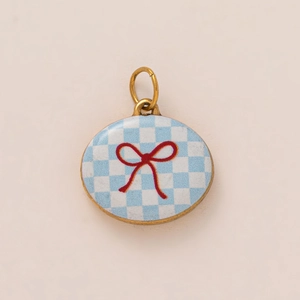 Detail of 18K gold-plated oval pendant featuring blue checkered pattern and red bow