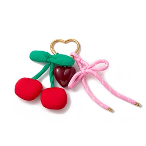 Nahaufnahme von roten Stoffkirschen und Herzanhänger mit rosa Schleife an Goldring