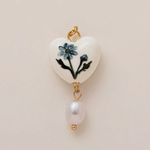 Détail d'un pendentif en céramique en forme de cœur avec motif floral bleu et perle blanche