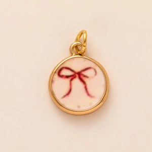 Macro view of a gold-plated round pendant featuring a hand-painted pink bow on a white inlay