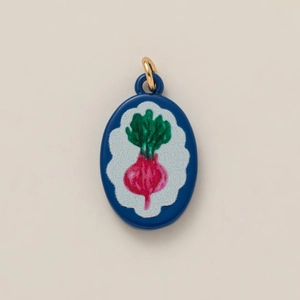 Detailed close-up of an oval enamel beet pendant with gold ring on beige background
