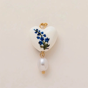 Detalle de un colgante de corazón de cerámica con motivos florales y perla blanca
