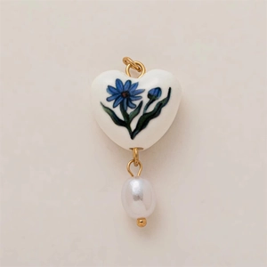 Vista detallada de un colgante de corazón cerámico con flores azules y una perla