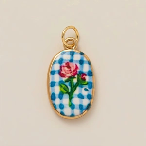 Detalle del colgante ovalado dorado con rosa roja sobre esmalte de cuadros azules