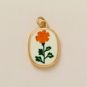 Vista macro de colgante ovalado dorado con textura de bordado floral naranja vivo
