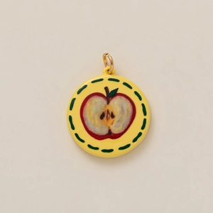 Detailed close-up of a round yellow enamel pendant featuring a hand-drawn apple motif