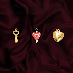 Gold heart locket, red enamel bead, and key pendants on a luxury red silk background