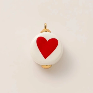 Dettaglio di ciondolo in ceramica bianca con cuore rosso e cappucci in metallo dorato