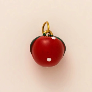 Macro detail of red apple fruit pendant with white polka dots and 18K gold ring