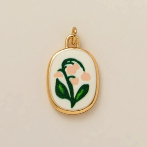 Détail d'un pendentif ovale doré avec motif de muguet sur fond en émail blanc poli