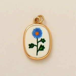 Détail du pendentif ovale plaqué or avec motif floral bleu sur insert blanc