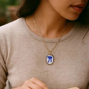 Detalle de un collar chapado en oro con un colgante de cerámica de lazo azul en una modelo