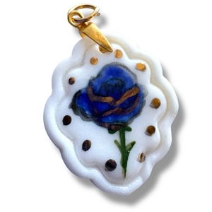 Detalle de un colgante de cerámica hecho a mano con rosa azul y bordes dorados