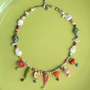 Artistic beaded pearl necklace featuring colorful vegetable and fruit pendants on green background