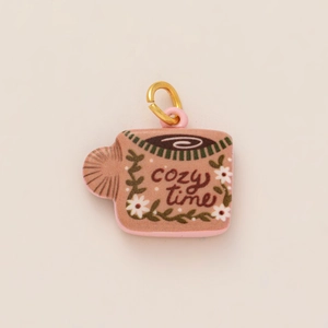 Detail van een roze mok sieraad hanger met cozy time tekst en gouden metalen ring