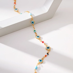 Chaîne dorée bohème avec pendentif œil bleu et perles colorées sur support minimaliste