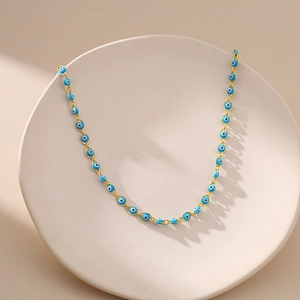 Dettaglio della collana dorata con ciondoli occhio blu su vassoio espositivo beige