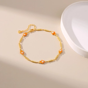 Détail d'une chevillère à billes dorées avec pendentifs Main de Fatma orange et œil